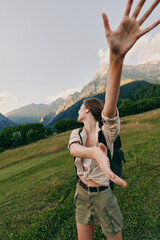 Fototapeta premium Cheerful woman outdoors reaching forward, sunlit moment, relaxed stance, fresh breeze, natural colors, scenic hillside with mountains in the background