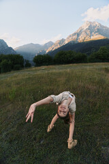 Fototapeta premium A young woman performs a backbend in an open meadow with distant mountains and clear sky, conveying balance, freedom and focus in a lifestyle moment.