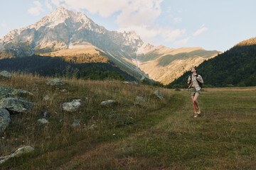 Fototapeta premium Lively woman hiking outdoors on a mountain meadow, backpack ready, sunlit trail, gentle breeze, vibrant nature, distant peaks, relaxed pose, lifestyle moment
