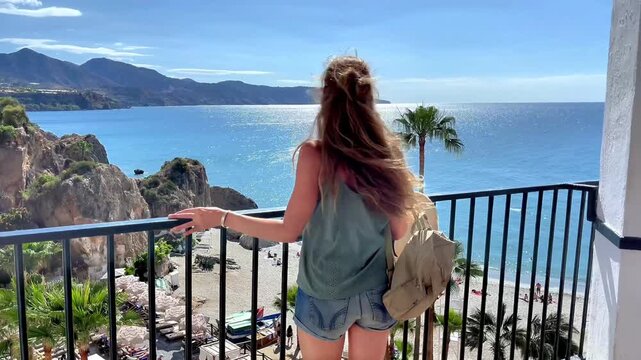 Rear view of woman tourist with backpack looking at mediterranean sea from a balcony, summer travel and vacation lifestyle concept, Malaga province in Spain, Nerja