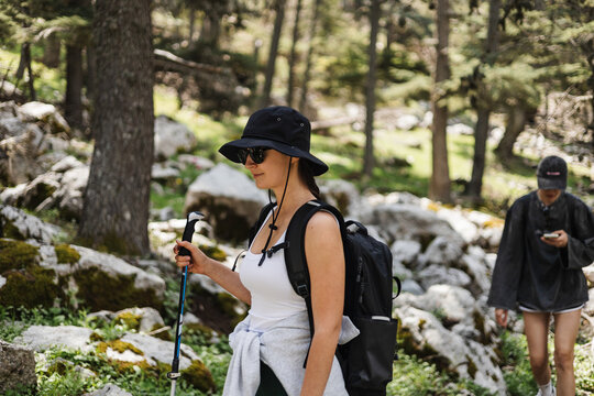 Woman hikes through forested area. She wears black hat and backpack.