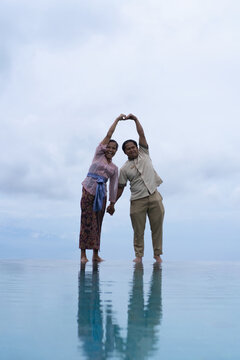 Joyful Balinese couple making heart shape at infinity pool, Bali