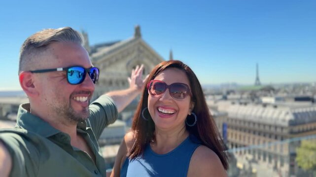 Happy multiracial couple with sunglasses taking a selfie video on a rooftop in Paris, France, enjoying their vacation with the city skyline and the Eiffel Tower in the background