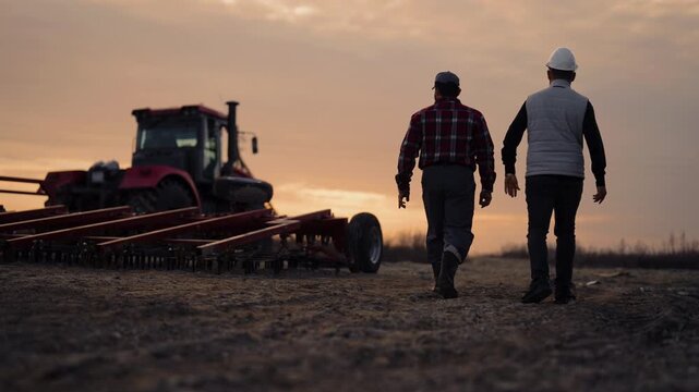 Agronomist and builder walking in fields, back view of people in farmland. Modern agricultural technology and machinery, innovation in agriculture, farmer and bioengineering examining farmland