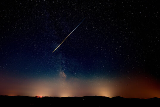 Constellation and Milky Way stars on a dark countryside skies with landscape silhouettes.