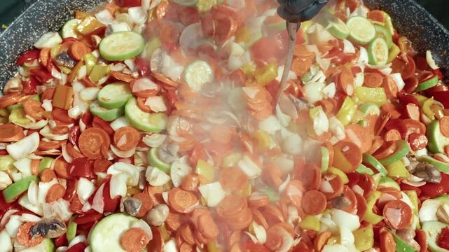 Colorful medley of chopped vegetables including carrots, bell peppers, onions, and zucchini sizzling in a large frying pan with steam rising, showcasing vibrant cooking process