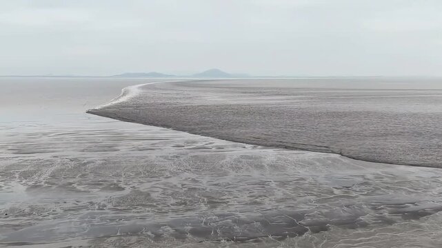 Spectacular aerial drone view of the rare fish scale tidal bore on the Qiantang River in China. The unique interlocking wave patterns form a scale-like texture on the water.