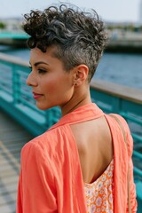 Fototapeta premium Elegant profile portrait of a woman with short curly hair in a coral jacket by the waterfront for branding and background design