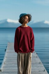 Obraz premium Young person standing on lakeside dock in casual sweater and beanie for portrait background and travel lifestyle banner