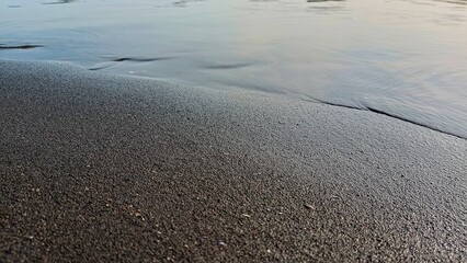 Abstract beach texture with calm water ripples and black sand shoreline, perfect for environmental, travel, and relaxation themes © Sarmiko.id