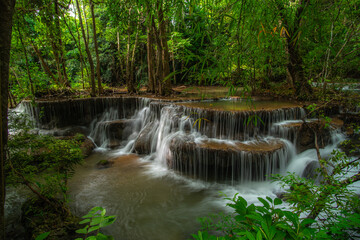 A turquoise waterfall cascades down in layers in the middle of the forest. © Pongsorn