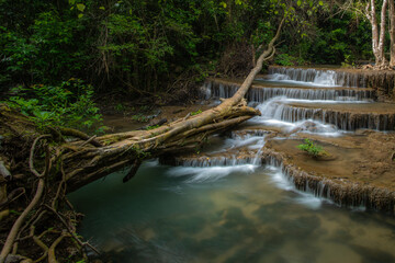 A turquoise waterfall cascades down in layers in the middle of the forest. © Pongsorn