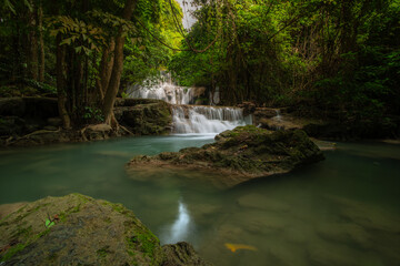 A turquoise waterfall cascades down in layers in the middle of the forest. © Pongsorn