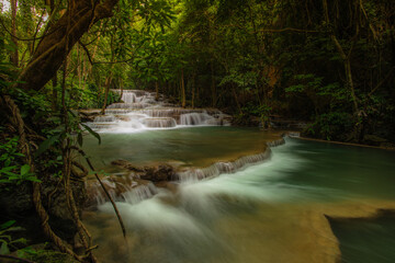 A turquoise waterfall cascades down in layers in the middle of the forest. © Pongsorn