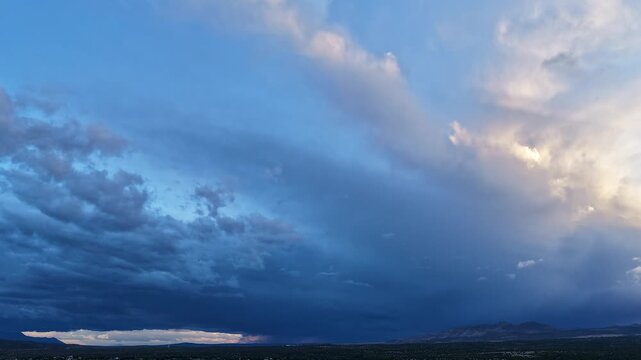 4K drone timelapse captures a fast moving blanket of blue and white clouds over a rugged mountainside at sunset. Cinematic atmospheric motion reveals shifting layers and soft twilight colors.