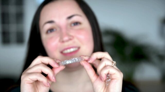Woman confidently presenting transparent dental aligner between fingers in natural indoor light, modern invisible orthodontic treatment and accessible dental care concept