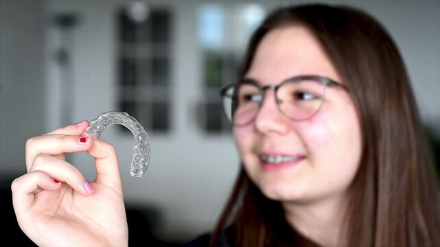 Teenager holding clear dental aligner and smiling confidently at home in natural light, adolescent orthodontic care and modern teeth straightening treatment concept