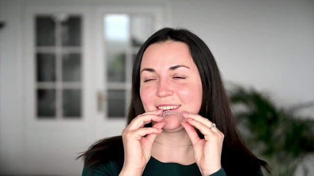 Woman confidently placing clear dental aligner onto teeth in home environment as part of daily routine, seamless invisible braces insertion and modern orthodontic self care