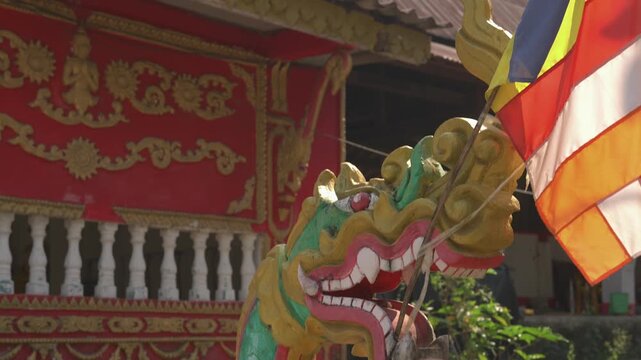 Close shot of a colorful dragon statue and Buddhist flag at Wat Khon Tai temple on Don Khon in Si Phan Don, Laos.