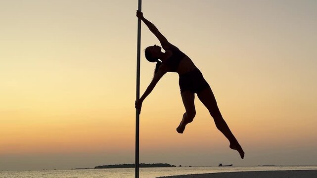 Woman performing pole dance move on beach at sunset near sea. Concept of fitness and graceful movement.