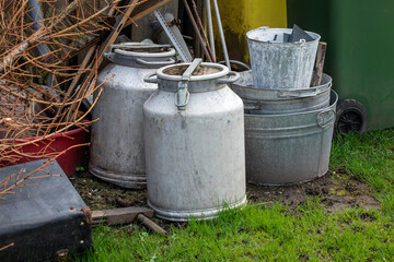 Obraz premium Old Metal Containers and Scrap Materials Stored Outdoors Near Garden Area
