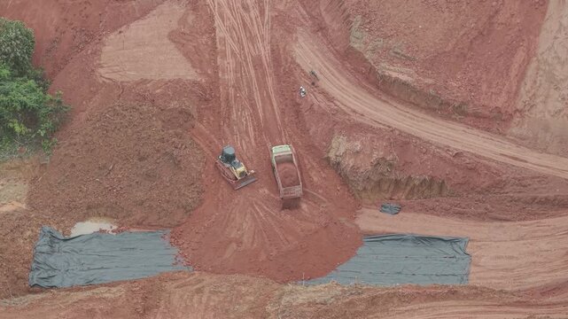 A crawler bulldozer is leveling the fill soil unloaded from a truck for road construction