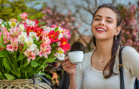 Woman drink coffee. Beautiful woman on a cafe enjoying morning with cup of coffee. She holds a cup, laughing, spring flowers