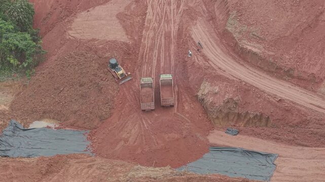A crawler bulldozer is leveling the fill soil unloaded from a truck for road construction