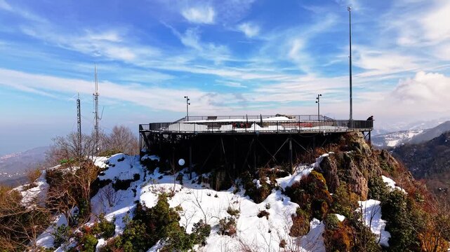 A professional 4K aerial shot flying closely over a snow-draped observation terrace. The camera glides past the platform to reveal a breathtaking and epic winter panorama of snow-covered mountain rang