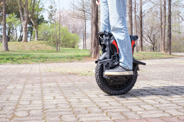A man in blue jeans and sneakers rides an electric unicycle in city park, side view. © TATIANA KIM