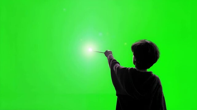 Young wizard boy casting spell over green screen background. School for wizards concept classroom chroma key. Bright magical light and expressive emotions in Halloween style scene. Copy space