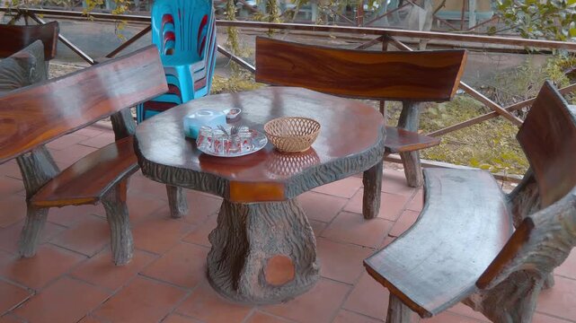 Shiny well polished table and benches made from solid mango tree wood on the terrace laid with natural red clinker tiles stand in garden with dry fruits served as treats for the guests on the table