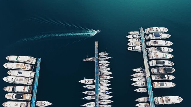 Aerial shot of speedboat cruising between Marmaris Marina docks leaving curved wake across deep blue harbor.