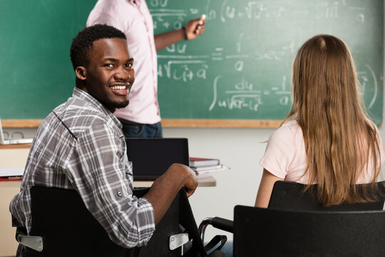 Smiling african american male student looking back in classroom during math lecture with formulas on chalkboard
