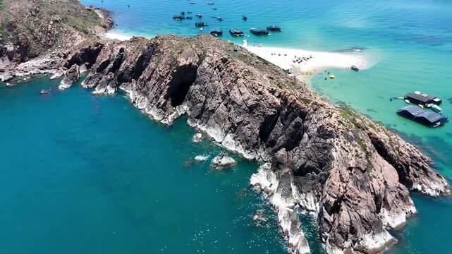 Aerial drone footage of Hon Kho Island in Quy Nhon, Binh Dinh Province, Vietnam. The drone reveals the island's dramatic rocky coastline surrounded by crystal-clear turquoise water, with traditional V