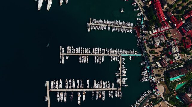 Aerial tracking shot of yachts and boats moored at marina of Gocek Turkey docks along coastal town waterfront with lateral pan.