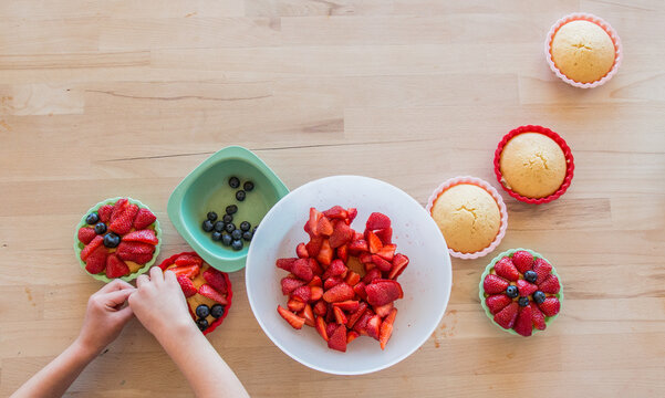 Child decorating a homemade cake with berries, close-up, from above, hands only