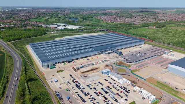 Aerial view of Symmetry Park, Kettering featuring a massive distribution warehouse with solar panels and extensive parking areas in Pytchley, England, United Kingdom.