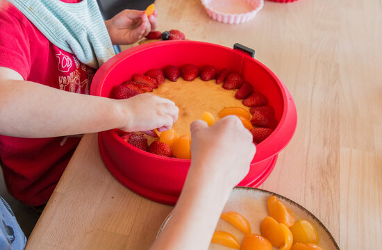 Children decorating a homemade cake with berries, close-up