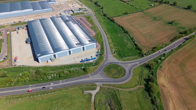 Aerial view of Symmetry Park logistics center with modern warehouses, a roundabout, and green fields in Pytchley, England, United Kingdom.