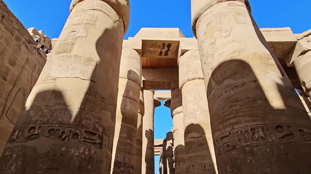 Karnak Temple in Luxor, Egypt. Massive hieroglyphic columns in Great Hypostyle Hall, Karnak Temple Luxor Egypt. Upward view of ancient carved pillars against blue sky.