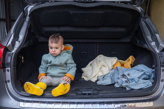 Toddler Sitting in Open Car Trunk in Garage.