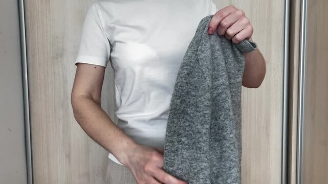 A woman carefully folds a warm wool sweater to put it in the closet. The coming of spring. The change of season, when heavy winter clothes give way to light and fresh clothes