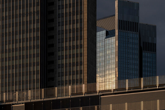 Across a Frankfurt district, golden light settles on glass architecture as an office building facade meets the shaded edge of a tower