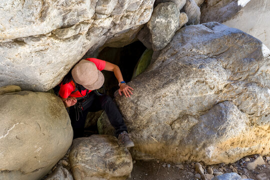 Female hiker squeezing through narrow rock opening in Sarakina Gorge, Crete, Greece