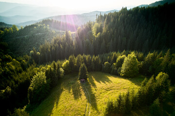 Fototapeta premium Breathtaking aerial view of mountain landscape at sunset. Golden light bathes rolling hills and lush forests, creating serene and idyllic scene. Distant mountains adding depth to picturesque vista.