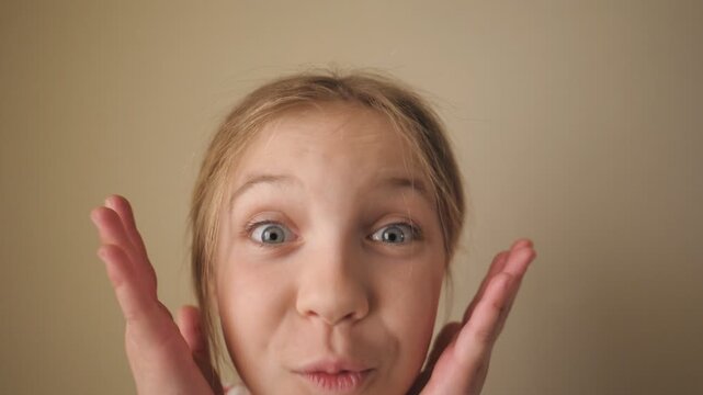 Happy little blonde girl looking into camera with wow expression indoor. Portrait of beautiful child showing surprise and amazement. Close up shocked female face of small kid inside. Slow motion