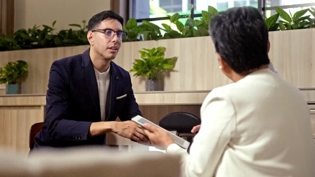 Two professionals converse in a modern office lounge; one gestures passionately while the other takes notes on a phone, reflecting a focused business consultation.