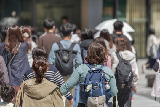 Diverse group of people move along sunny city street as a collective flow of bodies, unconsciously aligning their pace with those around them.