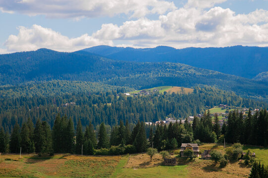 Picturesque mountain landscape. Ukrainian Carpathians. A cozy village lies in the valley below, surrounded by rolling green hills and misty mountain peaks. Bright traditional houses and untouched
